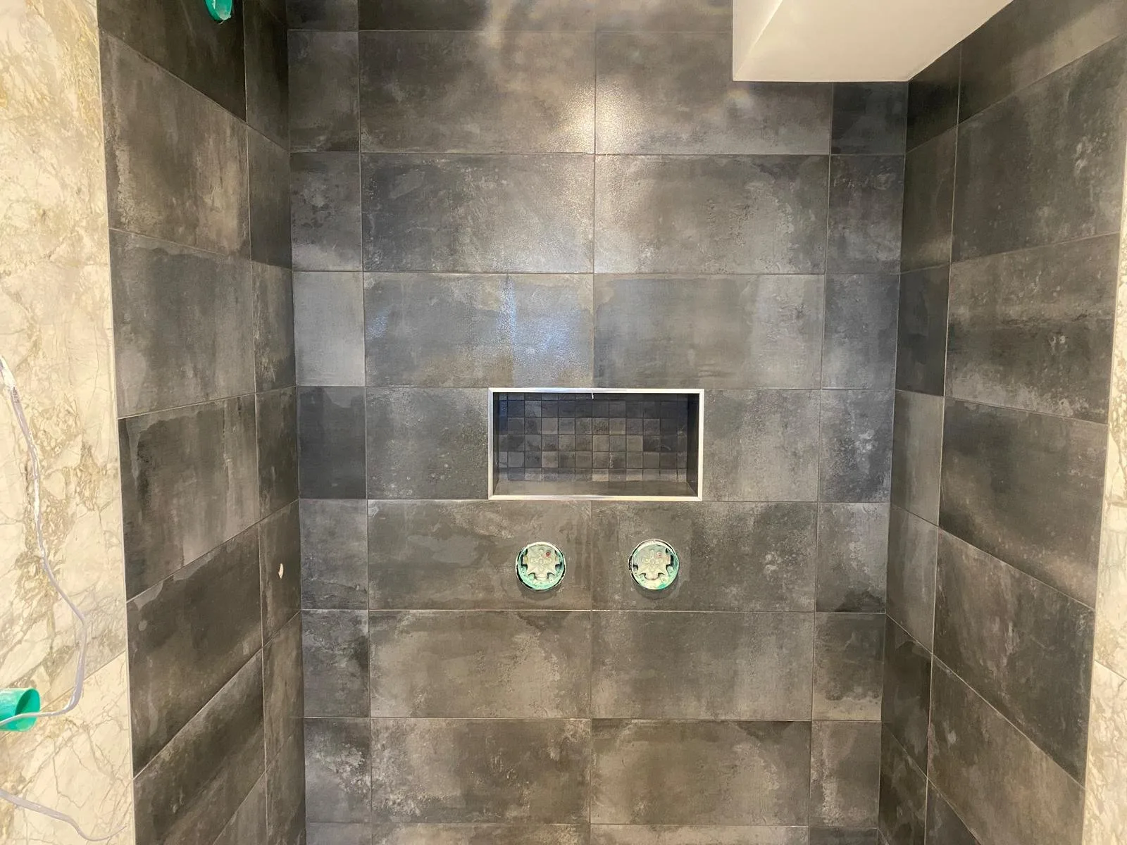 Dark grey concrete-effect tiled shower recess with a mosaic niche