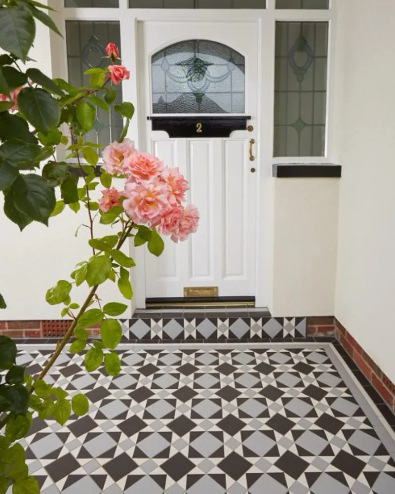 Victorian tiled porch floor in a black and grey star pattern, with a matching tiled step at a white front door